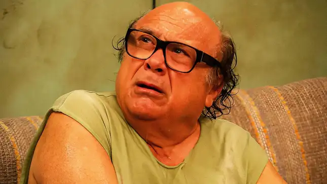 Danny DeVito sits on a couch.