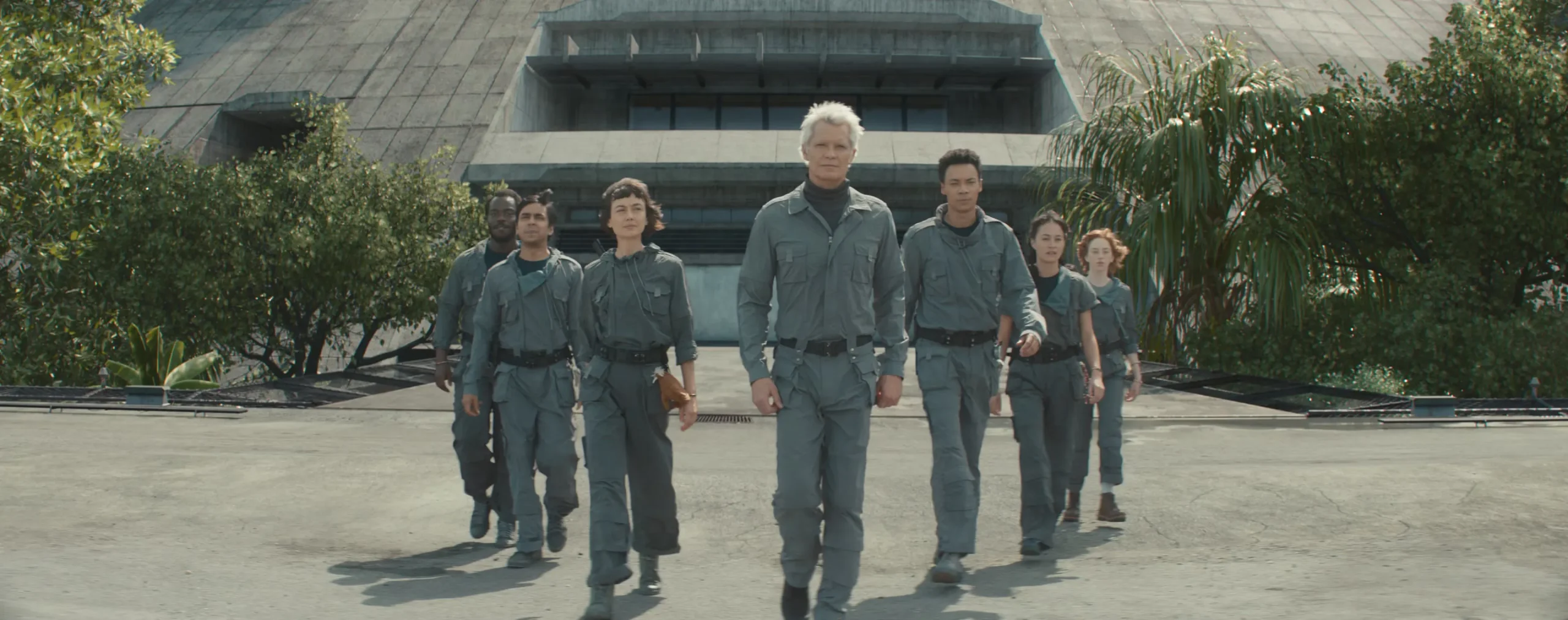 Kirsh (Timothy Olyphant, in a futuristic gray coverall), a human-looking android, leads a wedge of similarly dressed people out of a futuristic concrete bunker surrounded by trees in a scene from Alien Earth